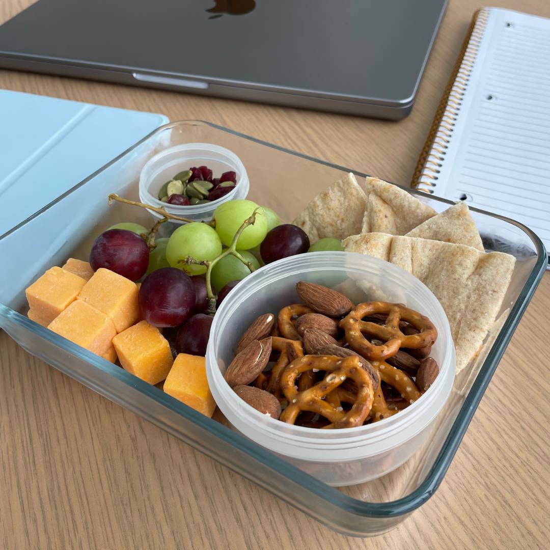 Homemade snack box with fruit, cheese and nuts around study material